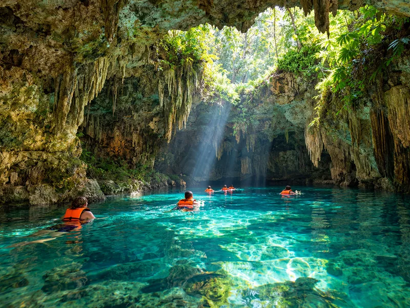 Schwimmer in Schwimmwesten, die durch eine sonnenbeschienene Höhle eines unterirdischen Flusses treiben